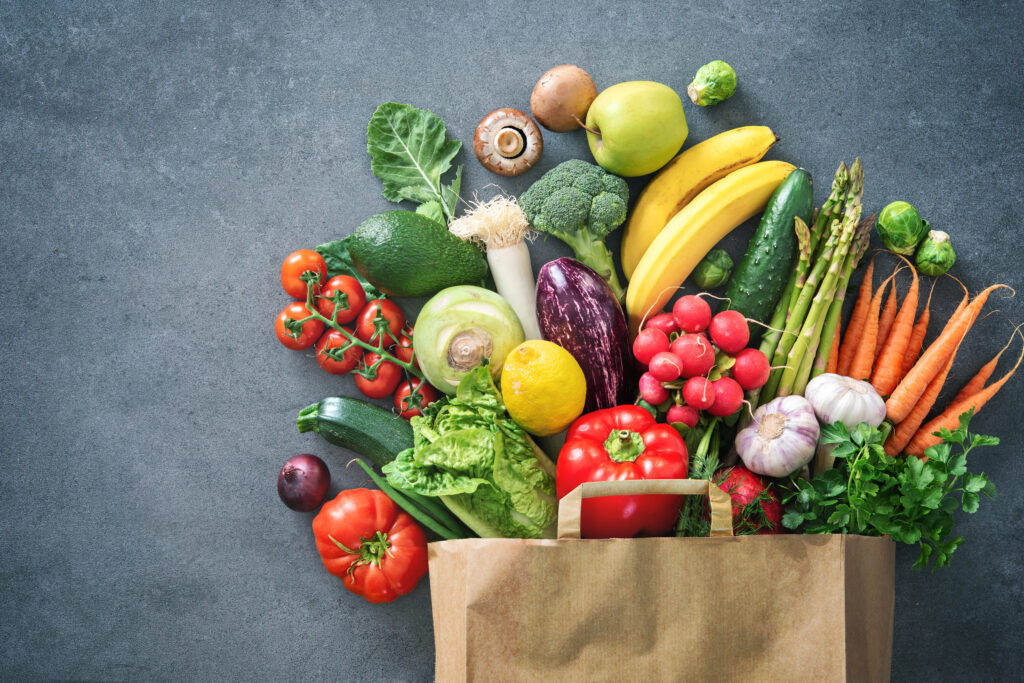 Shopping bag full of fresh vegetables and fruits laid flat on table table