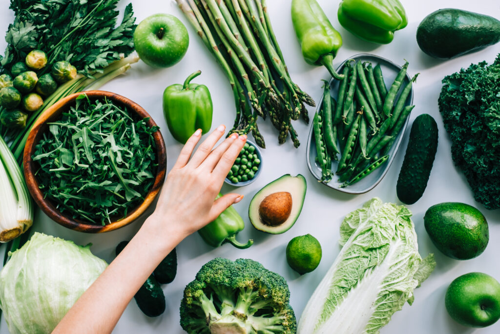 Woman's hands taking green peas from table with fresh green vegetables.