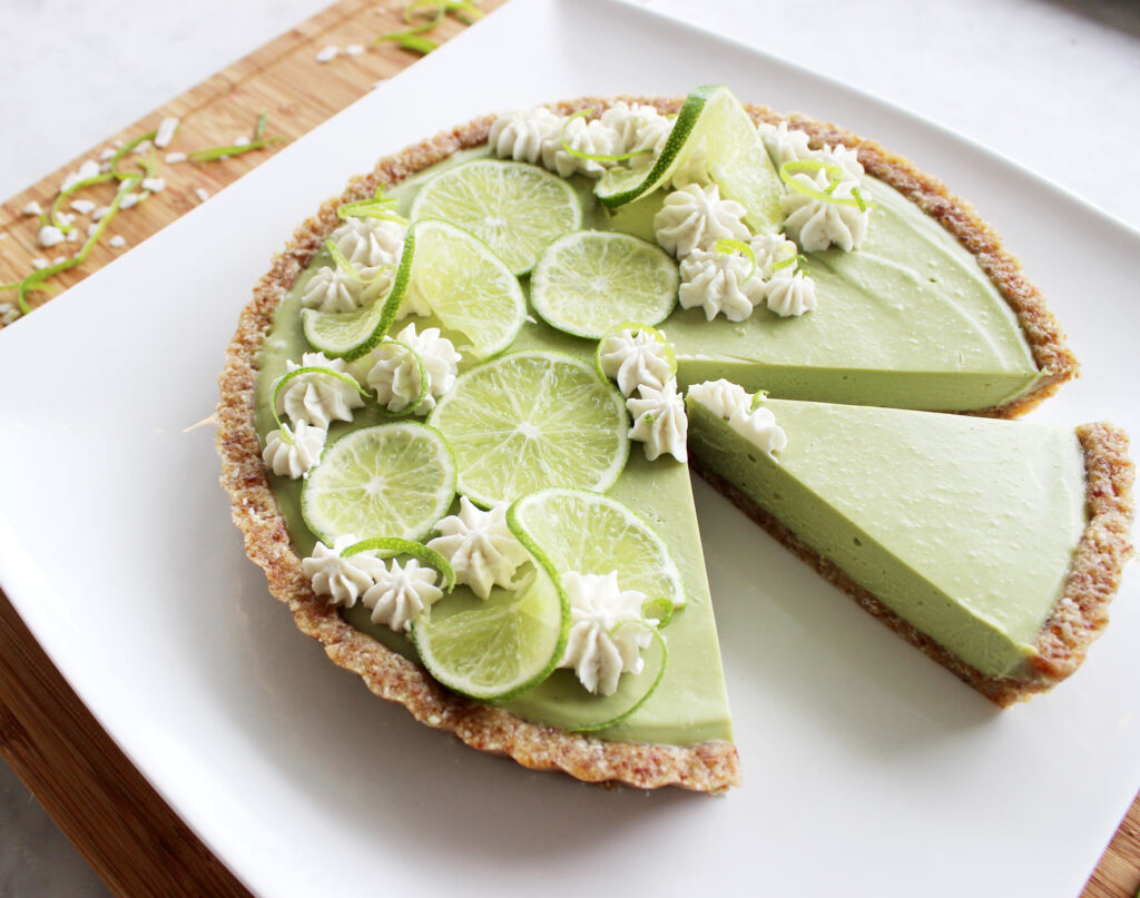 A stunningly decorated key lime pie sits on a plate, with a slice already taken out and another ready to serve.