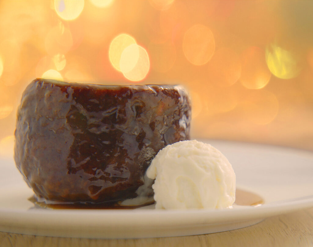 An individual sticky toffee pudding with a side of vanilla ice cream.