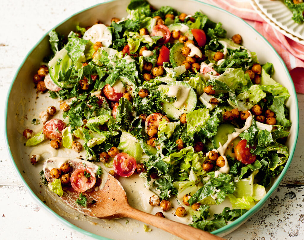 Image of a salad in a bowl with a wooden spoon. A serving appears to have been taken out.