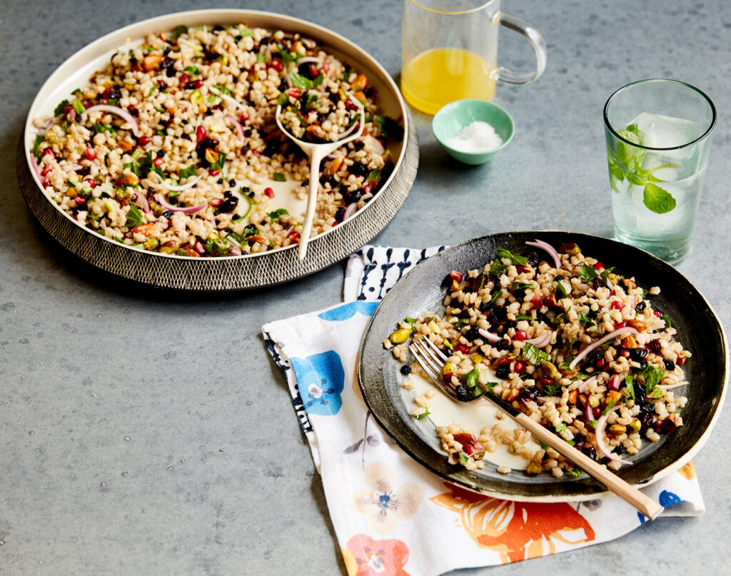 A serving bowl and plate of salad on a bench with drinks beside them.