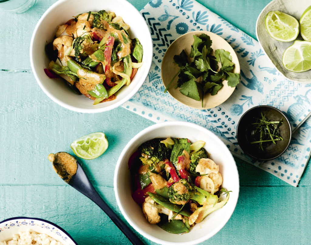 Overhead image of two serving bowls of veggie stir-fry in a red curry sauce. 