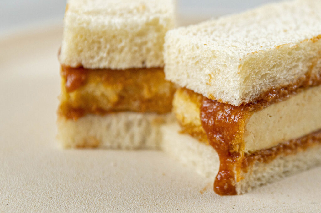 Two rectangular sandwiches with thick chunks of BBQ sauce-laden tofu, cut neatly with crusts off.