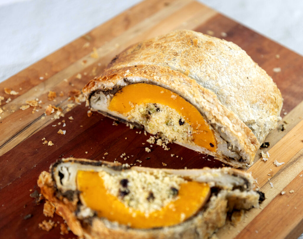 Image of a roast pumpkin wellington cut to reveal the centre, on a wooden chopping board.