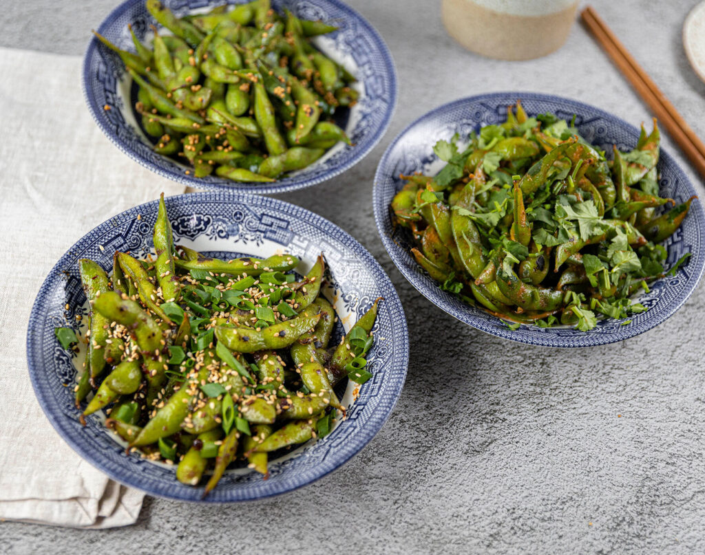 Three bowls of edamame displayed beautifully on a table setting, with chopsticks to the side.