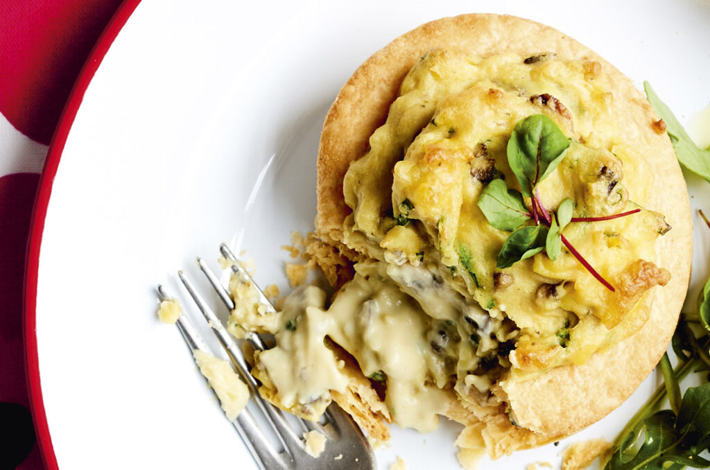 Close up of a flaky pastry vol-au-vent that has been broken with a fork to reveal the creamy white sauce filling with garlic and mushroom.