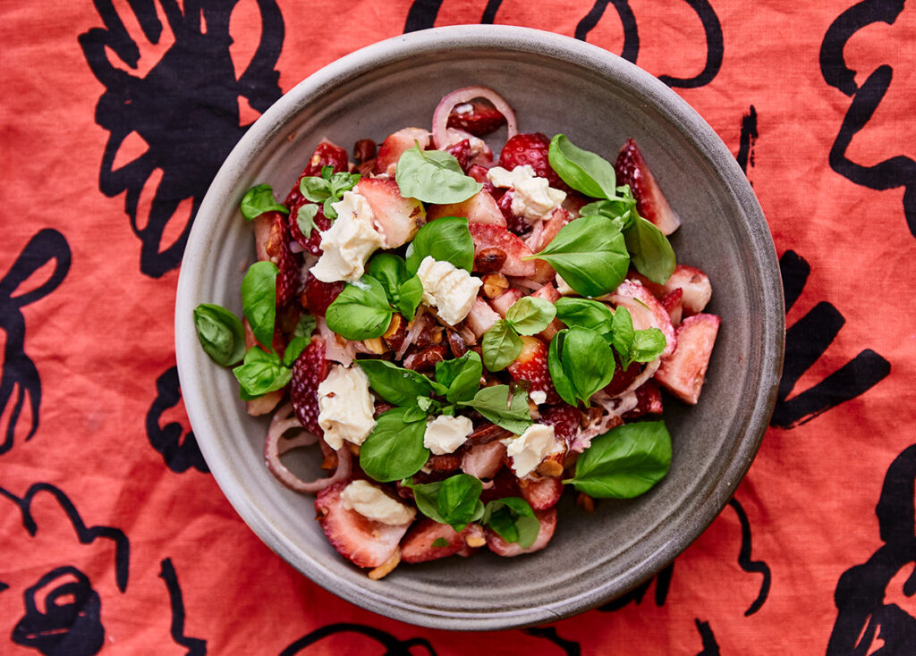 A vibrant green and red salad served in a bowl with a colourful red patterned background.