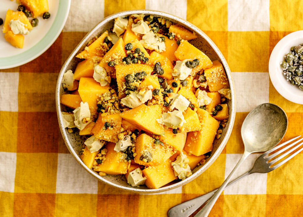 Overhead image of a Rockmelon Salad in a bowl on a plaid orange and white tablecloth.