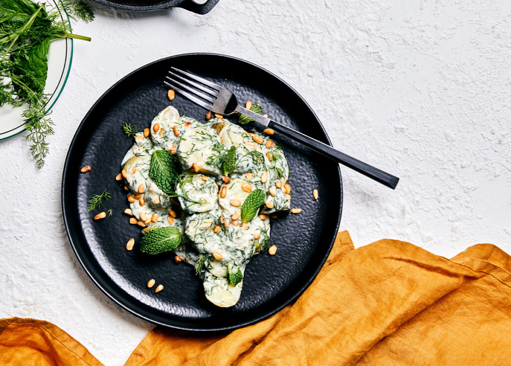 Overhead image of a creamy salad with charred cucumber and dill on a black stoneware plate.