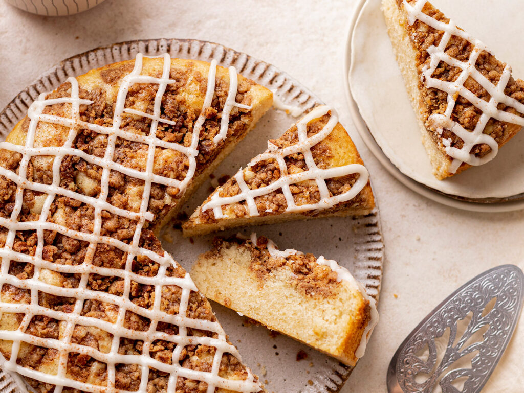 An overhead cropped image of a cinnamon tea cake, with several slices turned to the side to reveal a light and fluffy texture. It's beautifully decorated with a drizzle of white icing.