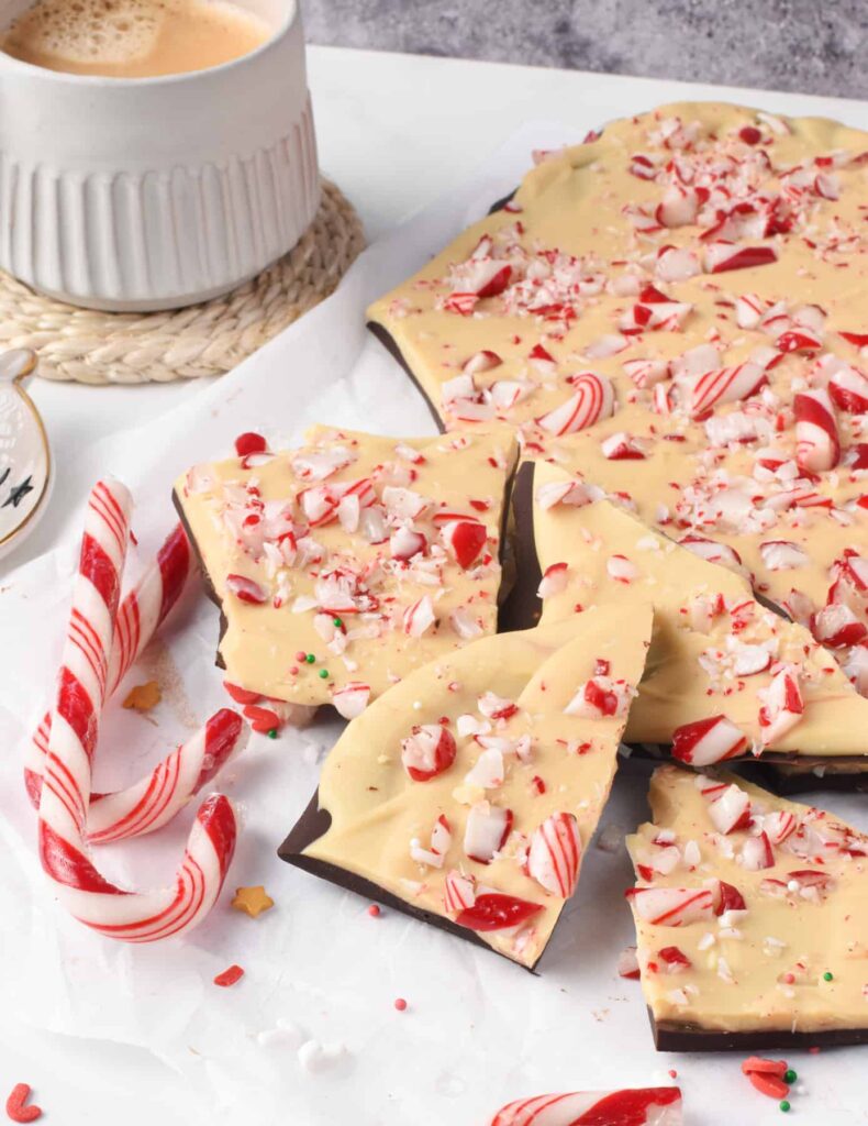 A full slab of peppermint bark, with some pieces broken off. The white chocolate side faces up with crushed candy cane topping. 