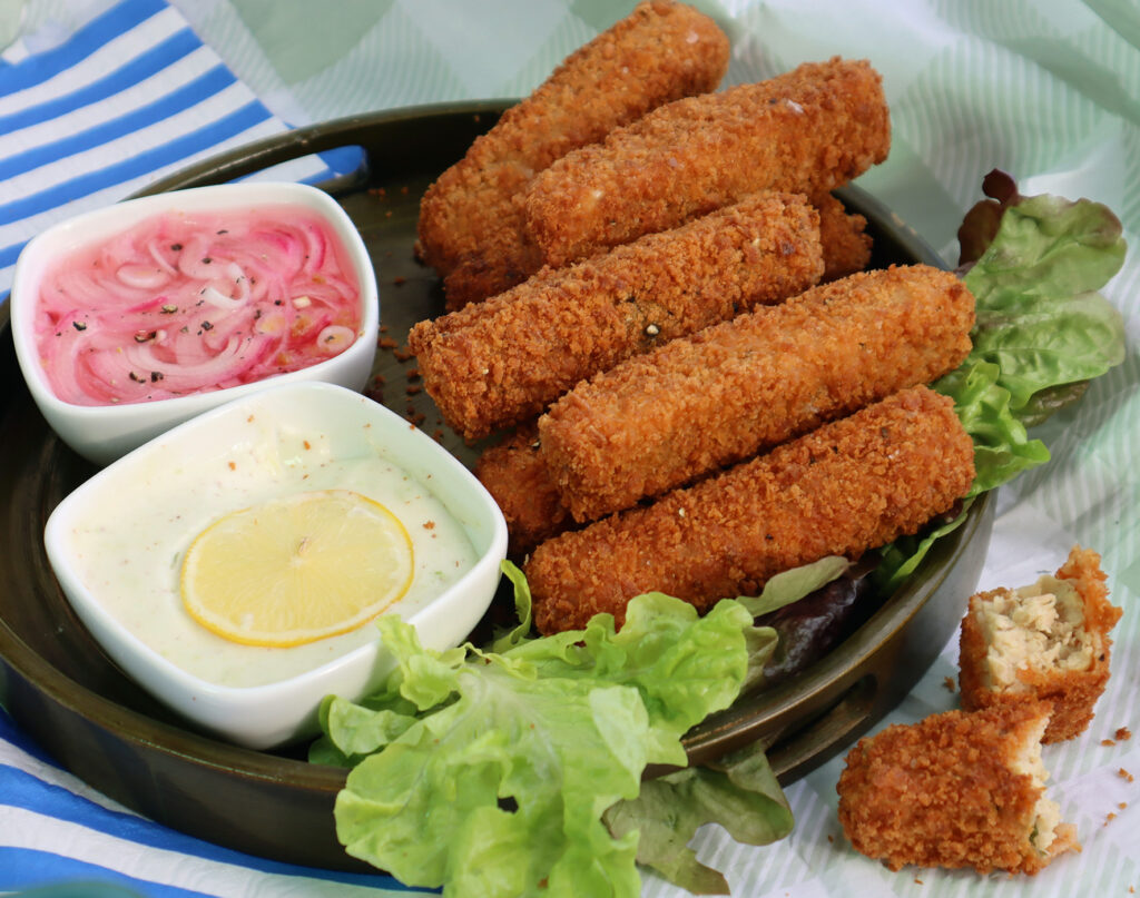 A plate piled high with vegan 'fish sticks' served on a bed of lettuce, with several condiments to the side.