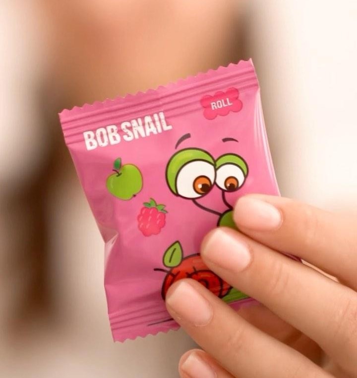 A close-up image of a hand holding to camera an individually wrapped Bob Snail fruit roll.