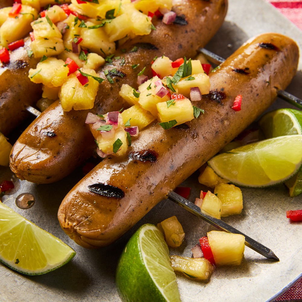 Close up image of chicken-style sausages skewered and topped with lime and pineapple.