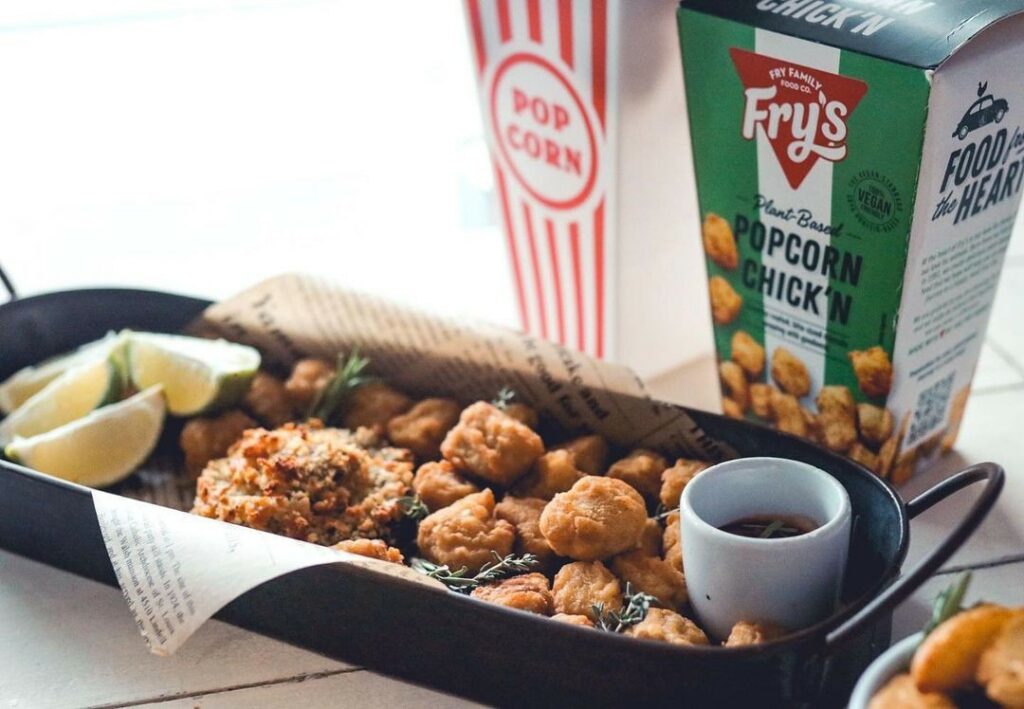 A serving platter full of popcorn chicken with a side of dippins sauce and lemon wedges.