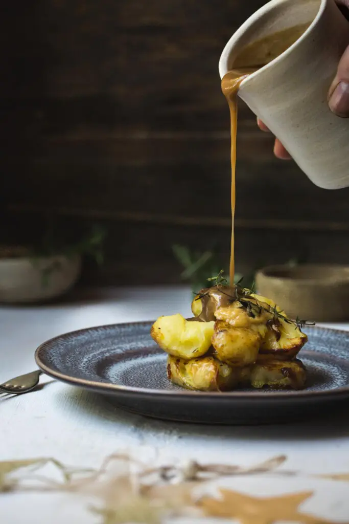 A side profile of potatoes on a plate, with a hand pouring gravy from above.