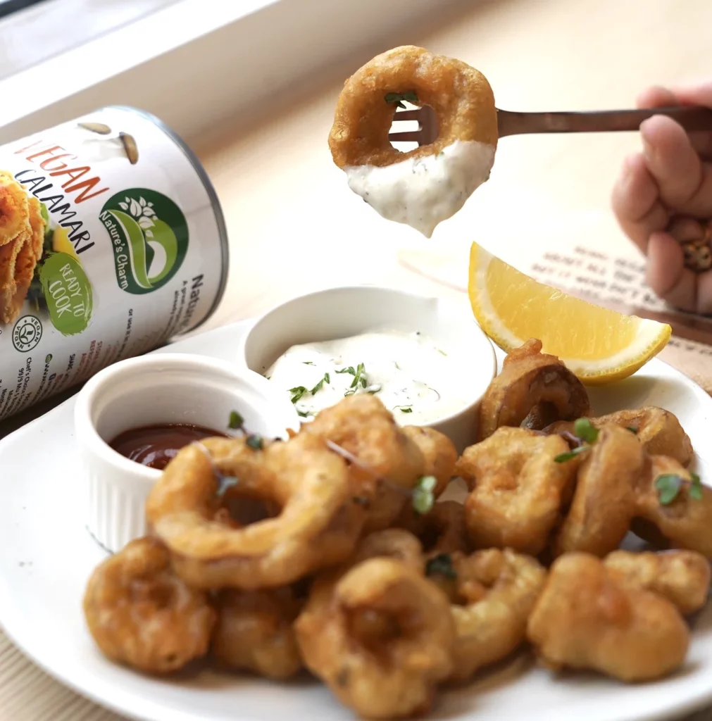 A hand reaching in to a plate piled with vegan calamari and dipping in a side of sauce.