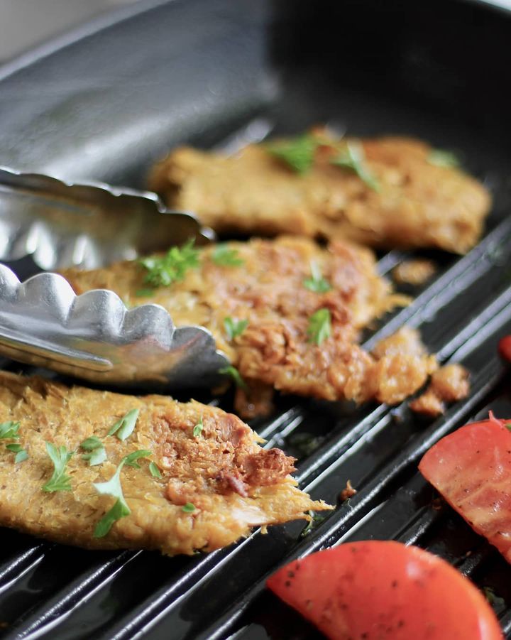 A close up of vegan chicken on a barbeque, with tongs reaching in to rotate.