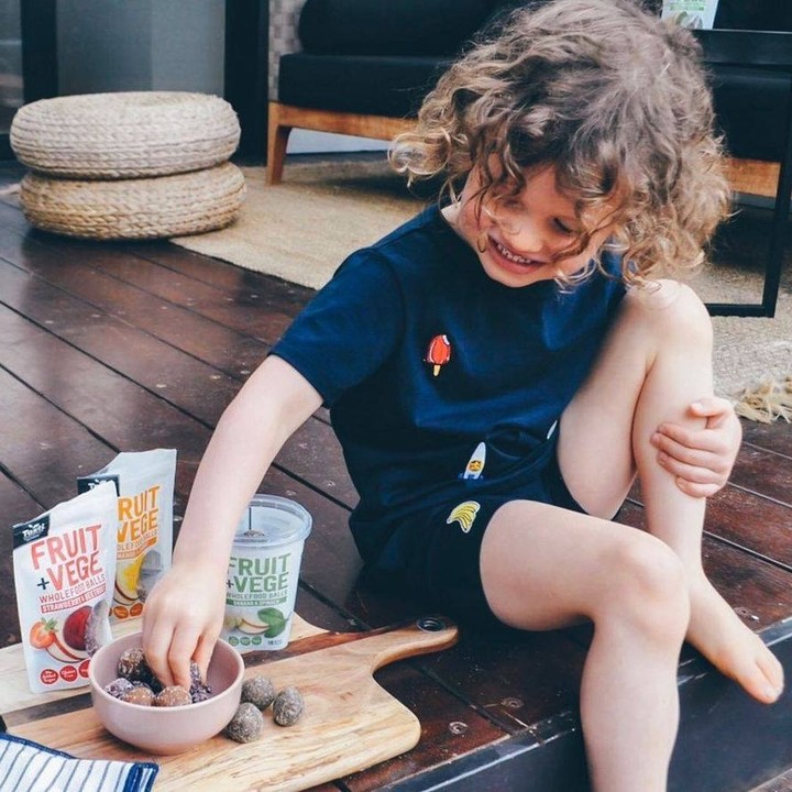 A child sitting outside on a deck reaching into a bowl of wholefood balls.