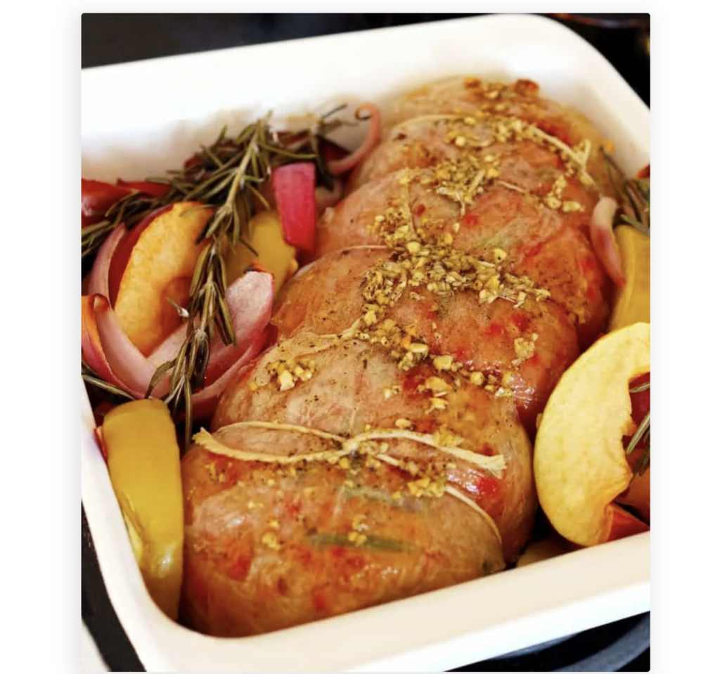 Image taken from above of a vegan pork tenderloin roast in an oven tray with slices of apple and onion.