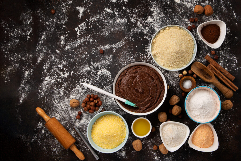 Baking staples sit on a black benchtop which is dusted with flour.