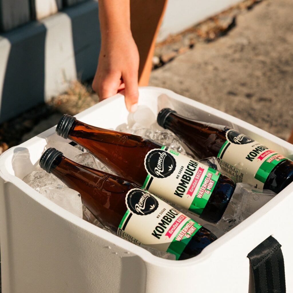 Three ice cold bottles of Remedy Kombucha sit in an open esky filled with ice.