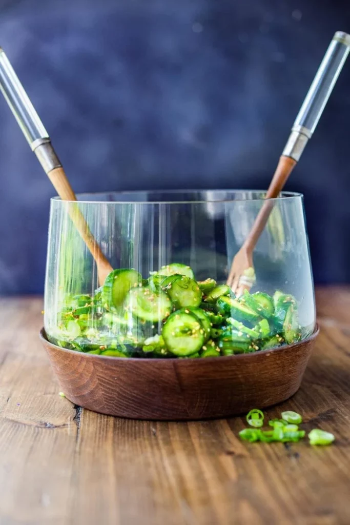 Image of Asian Cucumber Salad in a clear serving bowl with servers.