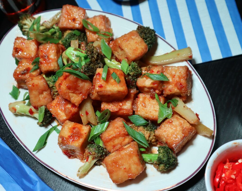 Sweet and spicy marinated tofu cubes are served with Asian greens. A side of fresh chilli slices sit beside the plate.