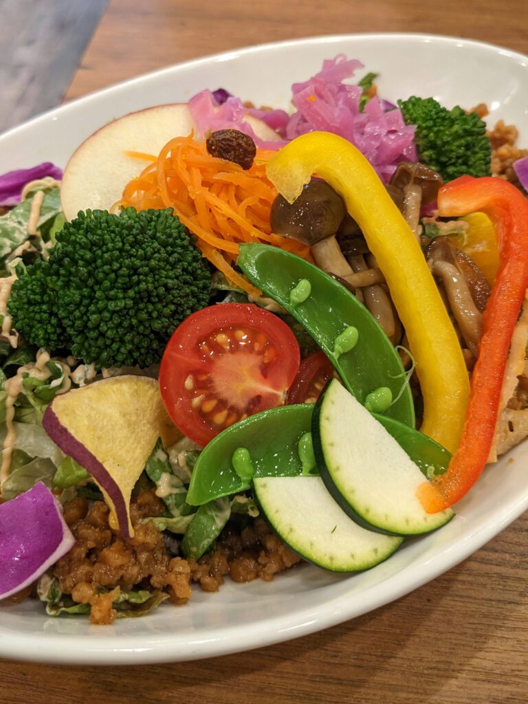 A hearty-looking rice bowl topped with vibrant, stir-fry style veggies, including zucchini, snow peas, cherry tomatoes, capsicum, broccoli, carrot, and purple cabbage.