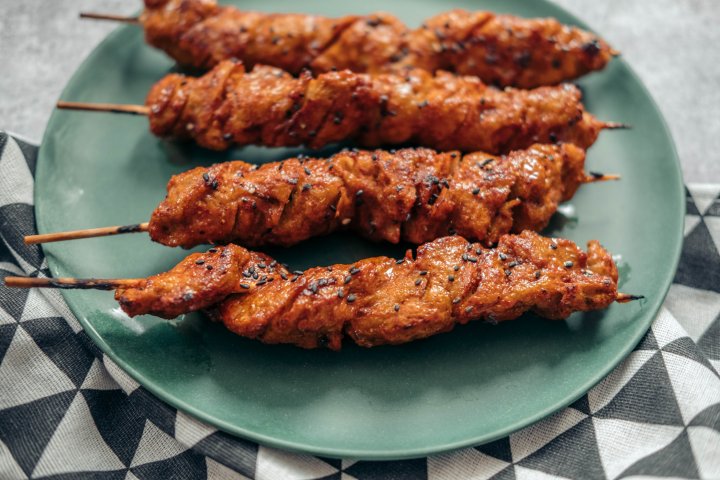 Four meaty looking skewer made from seitan on a green plate.