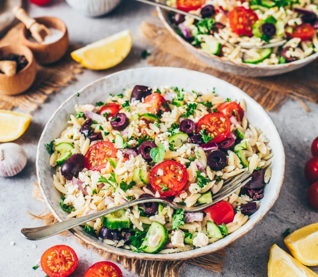 Gerek Orzo Pasta Salad served over two plates on a bench surrounded by ingredients.