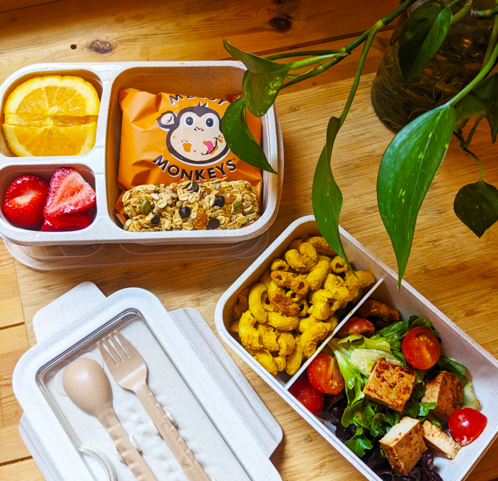 Overhead shot of an open lunchbox on a wooden bench, displaying a variety of plant-based and healthy treats.