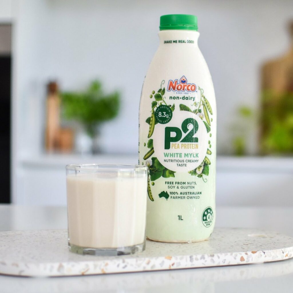 Image of a glass of milk on a bench next to a bottle of Norco non-dairy milk made with pea protein.