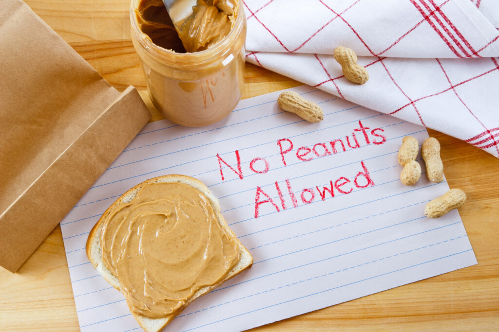 Overhead view of peanut butter on bread with red crayon warning against peanuts which are a dangerous allergen for many children and adults.