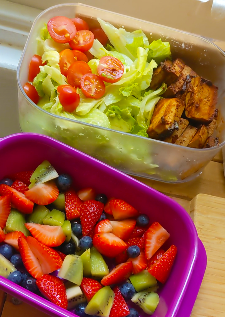 An overhead image of two pre-prepared salad in containers, one fruit mix and one tofu, lettuce and cherry tomato mix.