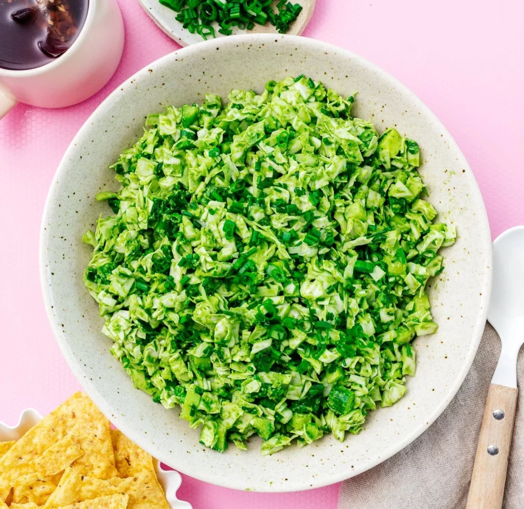 A vibrant green salad in a bowl. finely diced, sitting on a pink tablecloth.