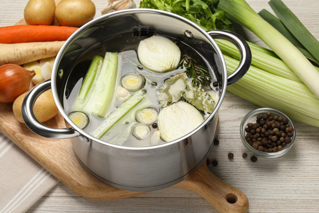 Pot and different ingredients for cooking tasty bouillon on white wooden table