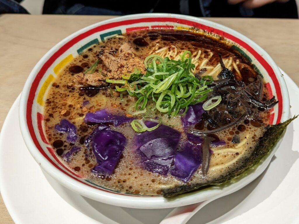 A large bowl of vegan tonkotsu-style ramen, garnished with spring onions, red cabbage, and nori.