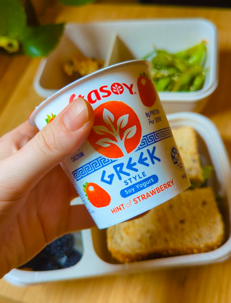 A close-up of a strawberry soy yoghurt tub held to camera.