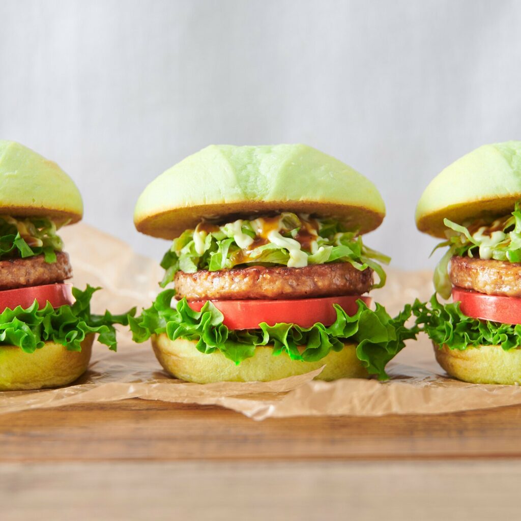 An image of three Green Teriyaki Burgers sitting on a board.