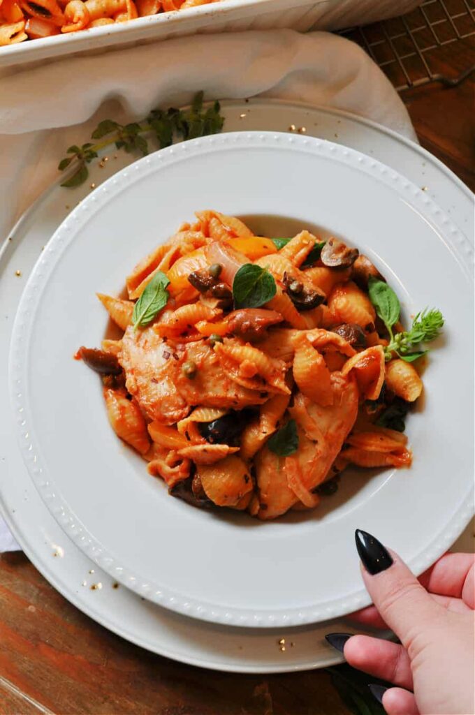 Overhead image of a hand reaching in to grab a bowl of delicious looking vegan 'chicken' cacciatore.