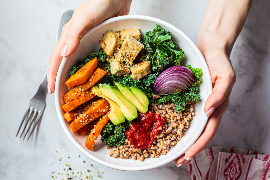 Vegan lunch salad with kale, baked sweet potato, tofu, buckwheat and avocado in a white bowl.