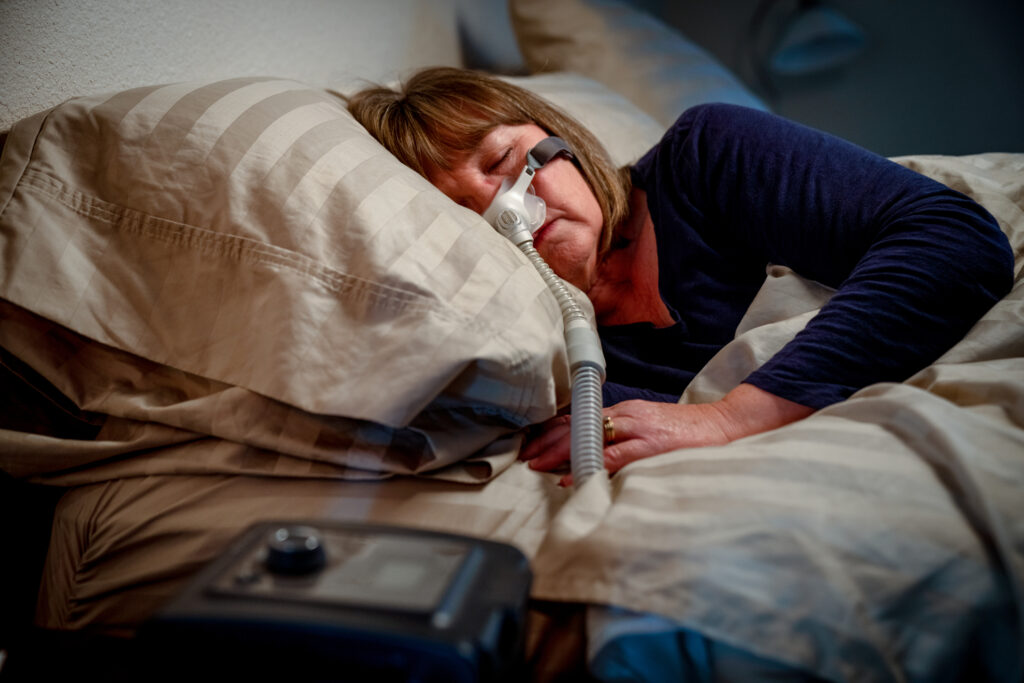 Woman asleep in bed using a CPAP machine to provide therapy for sleep apnoea.