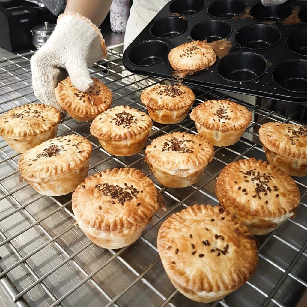 A baker is placing a dozen hot pies from the oven straight onto a wire rack.