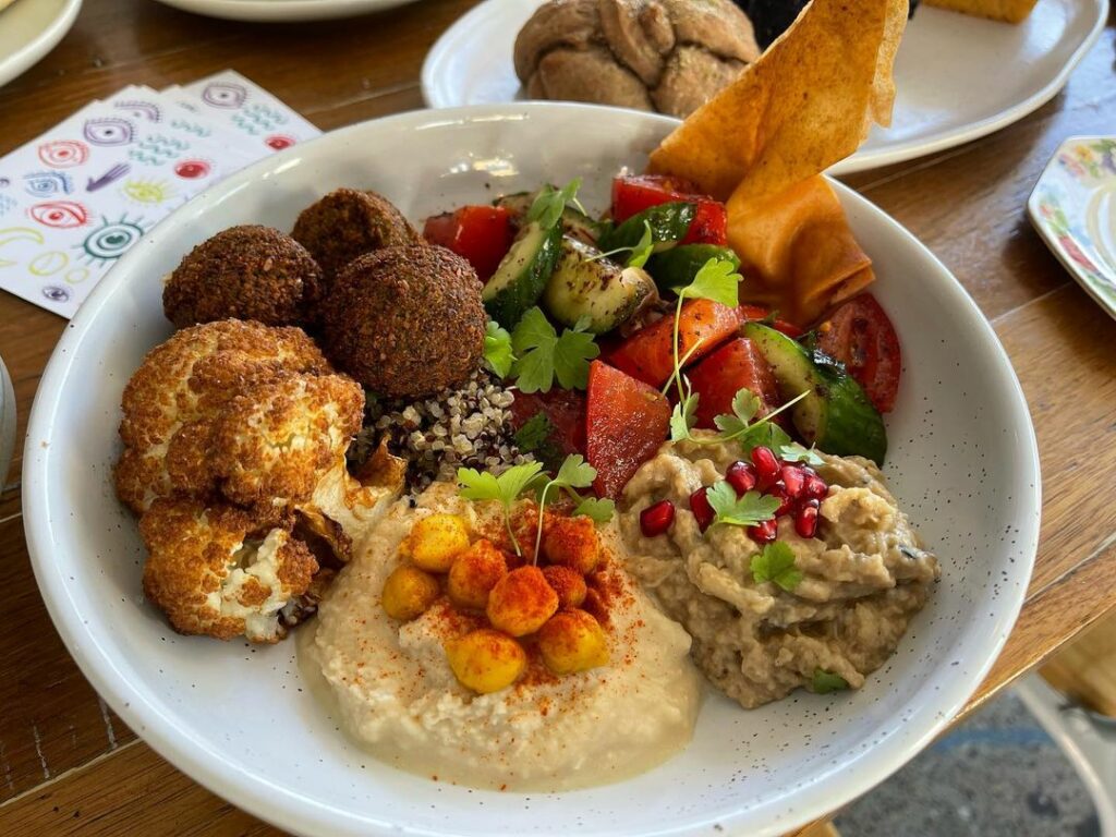 A dish on a table with traditional Palestinian fare, including falafel, hummus, salad, and some crispy cauliflower.