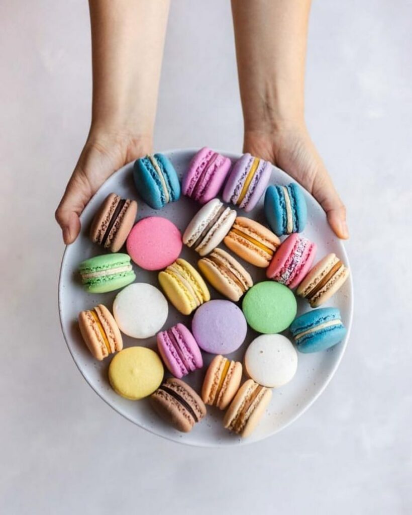 An overhead shot of outreached arms holding a plate of colourful vegan macarons.