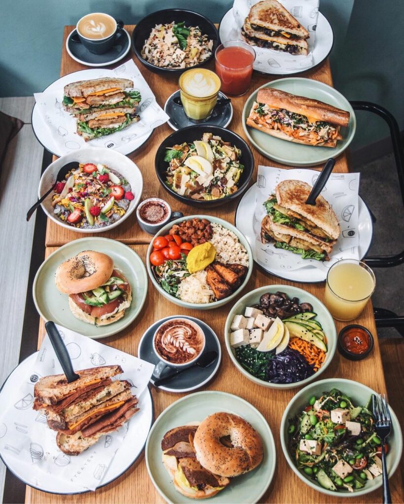 An overhead image of a full table spread at Shift Eatery, showing bagels, toasties, salads, baguettes, coffees, juice and more.