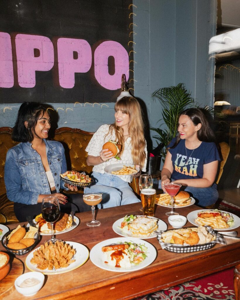 Three friends dine inside the pub with a table full of traditional pub fare made vegan,