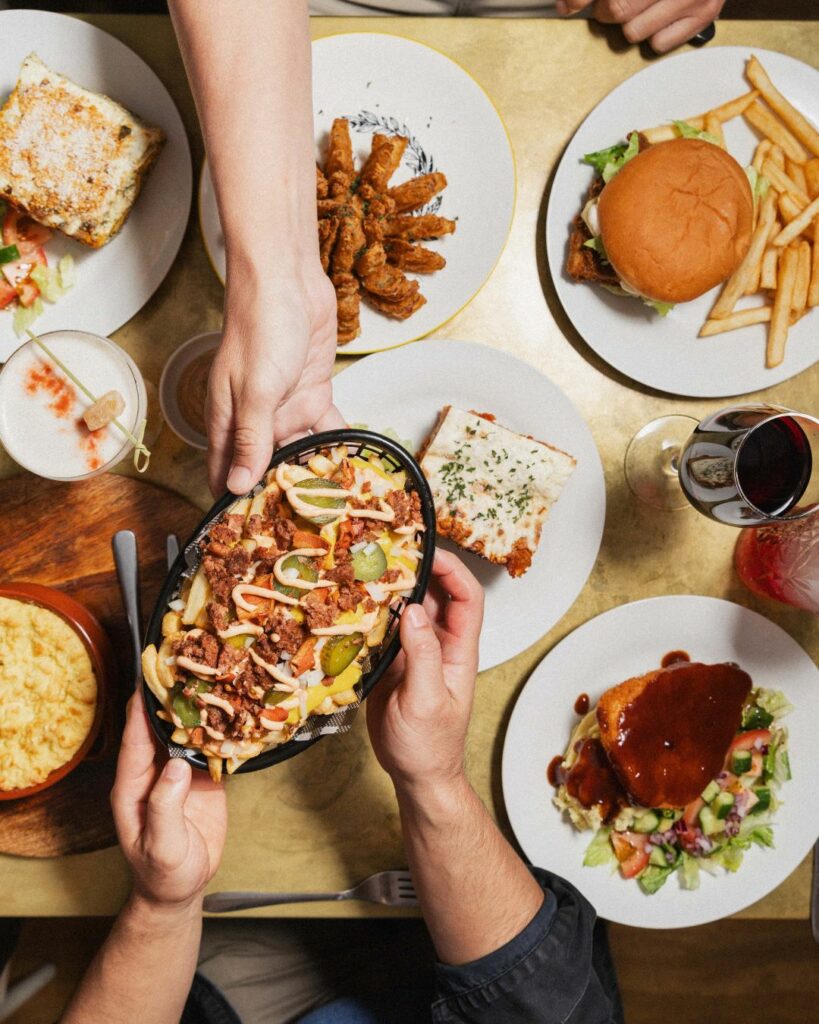 An overhead image of a table full of classic pub fare made vegan. A hand is reaching over to a dish that is being passed.